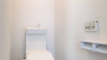 A small, white bathroom with a toilet, a wall-mounted heater, and a wooden floor.