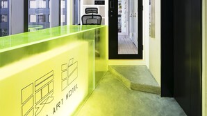 A modern hotel reception area with a bright yellow counter, a black door, and a view of the cityscape through large windows. - MANGA ART HOTEL, TOKYO - Hostel (Tokyo)