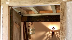 Ein rustikaler Raum mit Holzbalkendecke, einem Bett mit gelber Decke, einem hängenden Vogelkäfig und einer Wandleuchte.