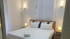 Un lit bien fait, avec des draps blancs et deux oreillers, une lampe de chevet de chaque côté et une serviette enroulée posée sur le lit.