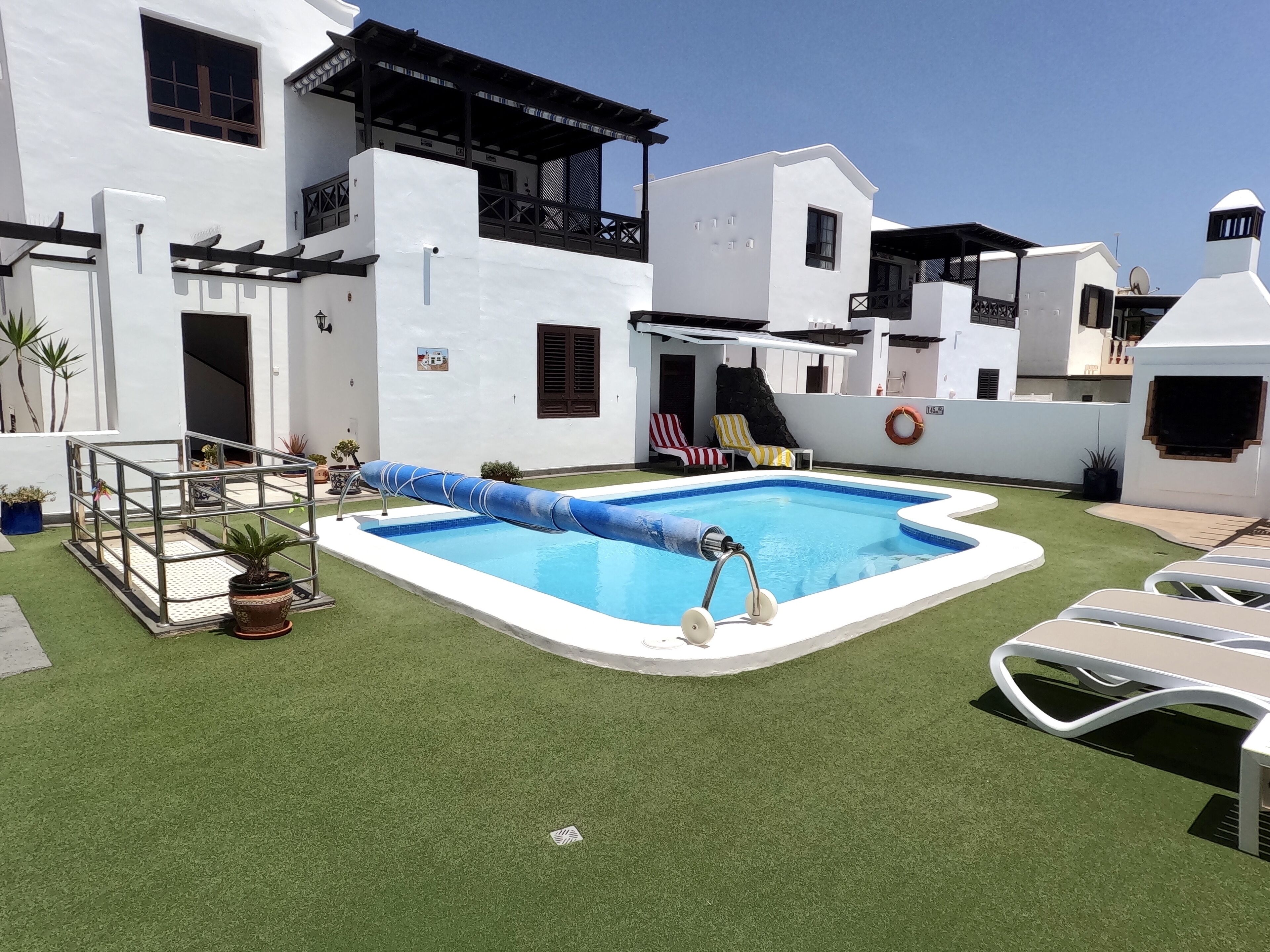 A swimming pool with a slide, surrounded by a white building with balconies and a small deck area.