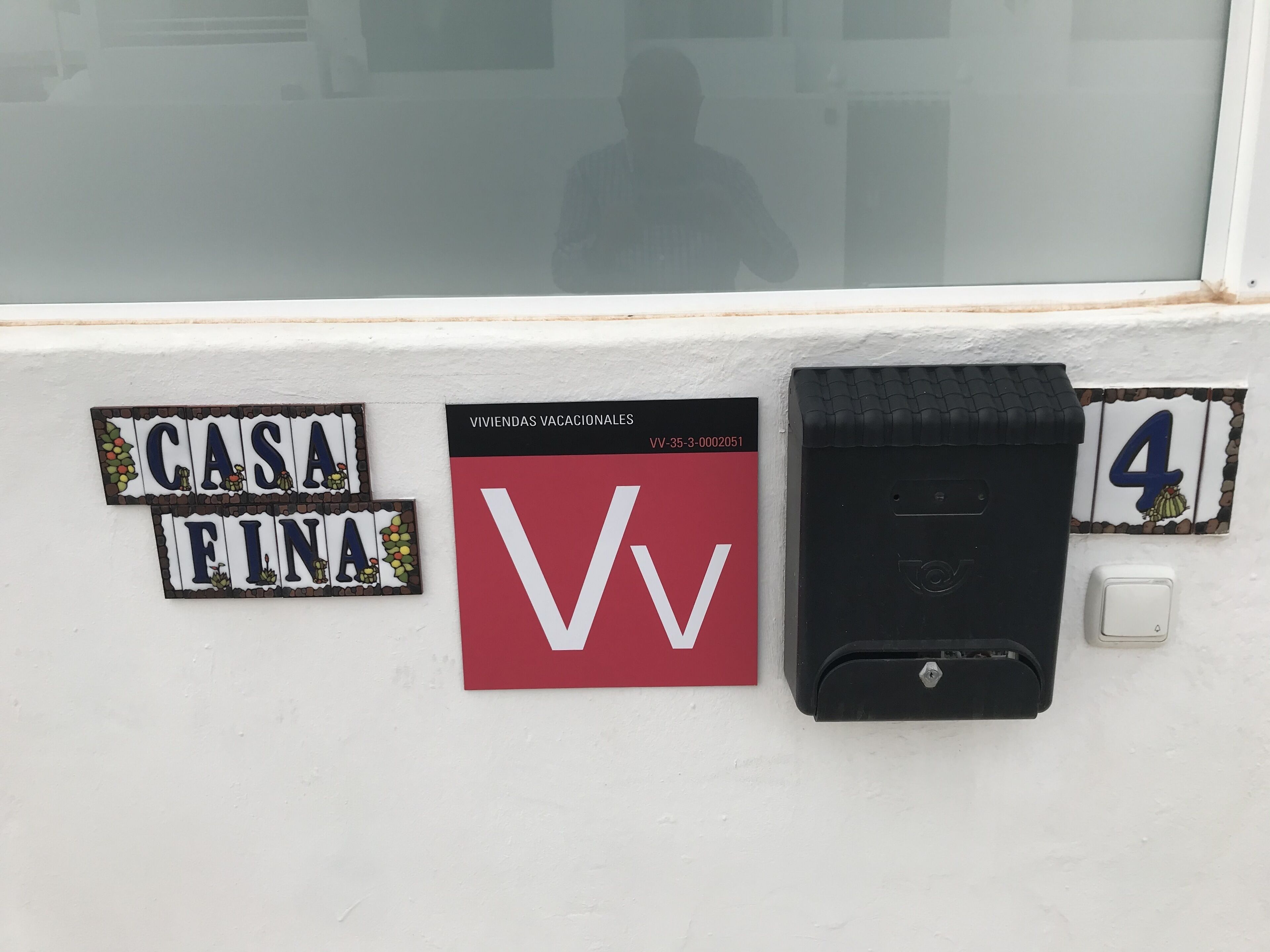 A wall with a nameplate reading 'CASA FINA,' a red sign with 'VV' and a number '4,' and a black mailbox.