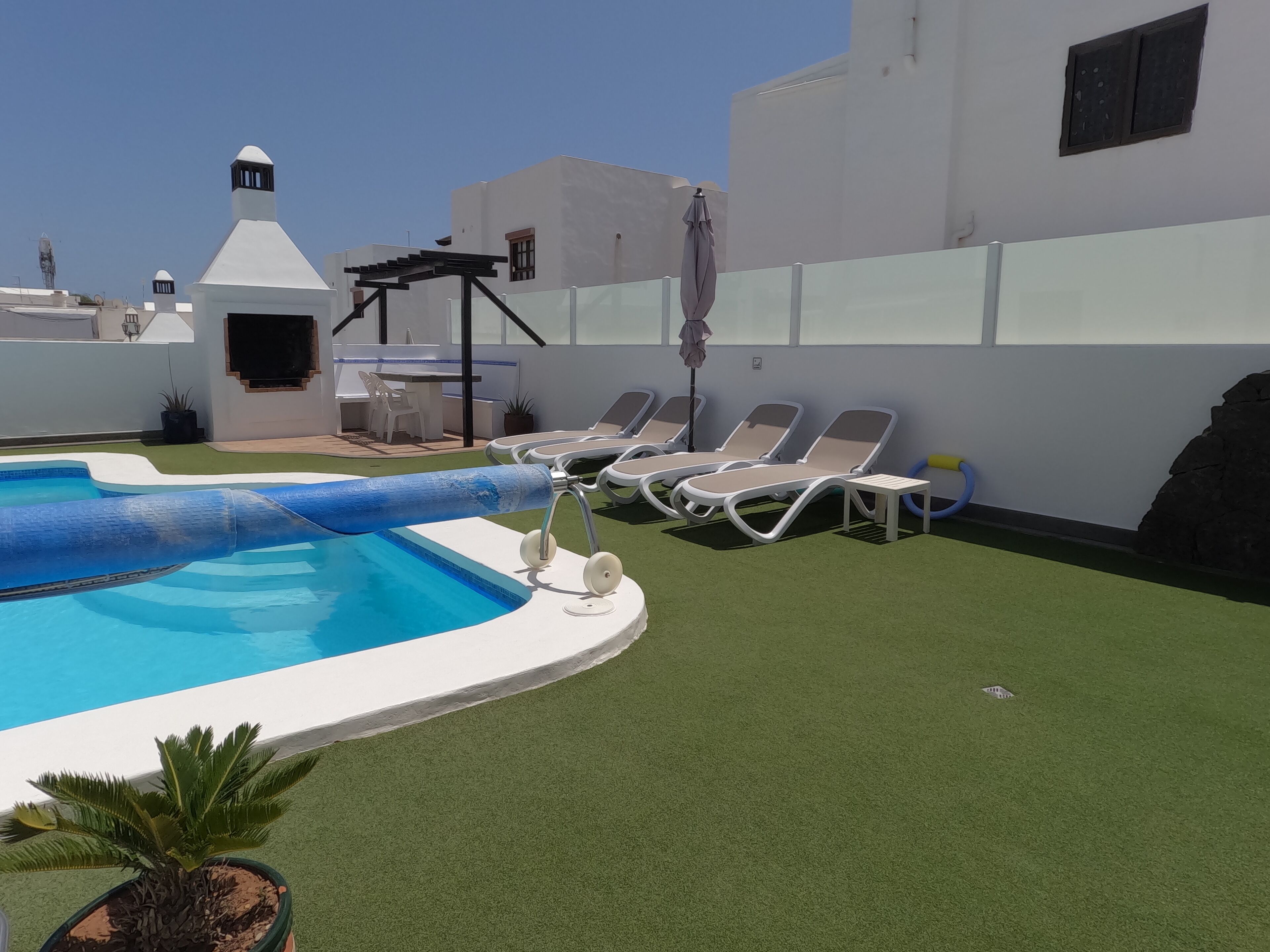 A rooftop pool with artificial grass, lounge chairs, and a pergola.