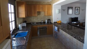 A compact kitchen with wooden cabinets, a built-in oven, a sink, and a countertop with a water dispenser. - Fabulous Detached Villa in Premier Location, Full Air Con, Heated Pool, Wi-Fi + (Puerto del Carmen)