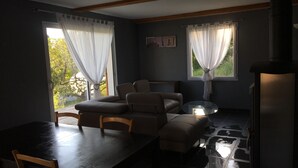 A cozy room with a dark wooden table, two cushioned chairs, and a glass coffee table. There are two windows with sheer curtains, and a painting on the wall. - Contemporary cottage between Ubaye and Durance overlooking the lake of Serre Ponçon 2 (Le Sauze-Du-Lac)