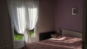A bedroom with a bed, a nightstand, a lamp, a window with curtains, and a wall-mounted light switch. - Contemporary cottage between Ubaye and Durance overlooking the lake of Serre Ponçon 2 (Le Sauze-Du-Lac)