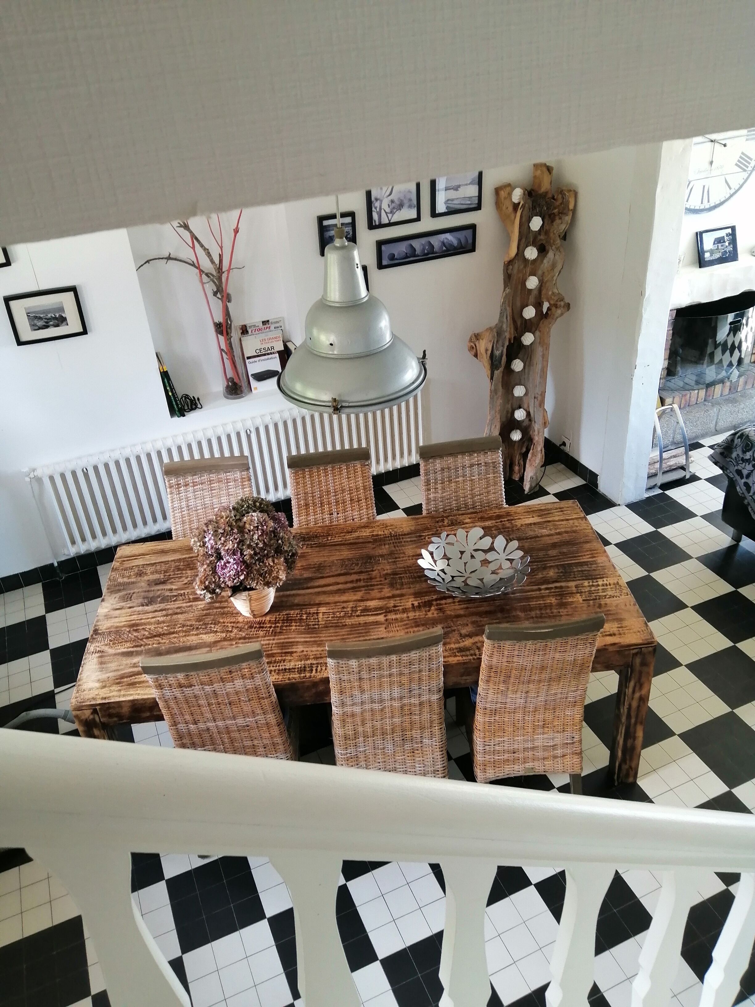 A dining area with a wooden table and wicker chairs, a decorative wall piece, and a radiator.