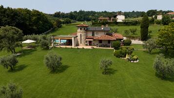 Una casa grande con piscina, rodeada de césped cuidado y árboles.