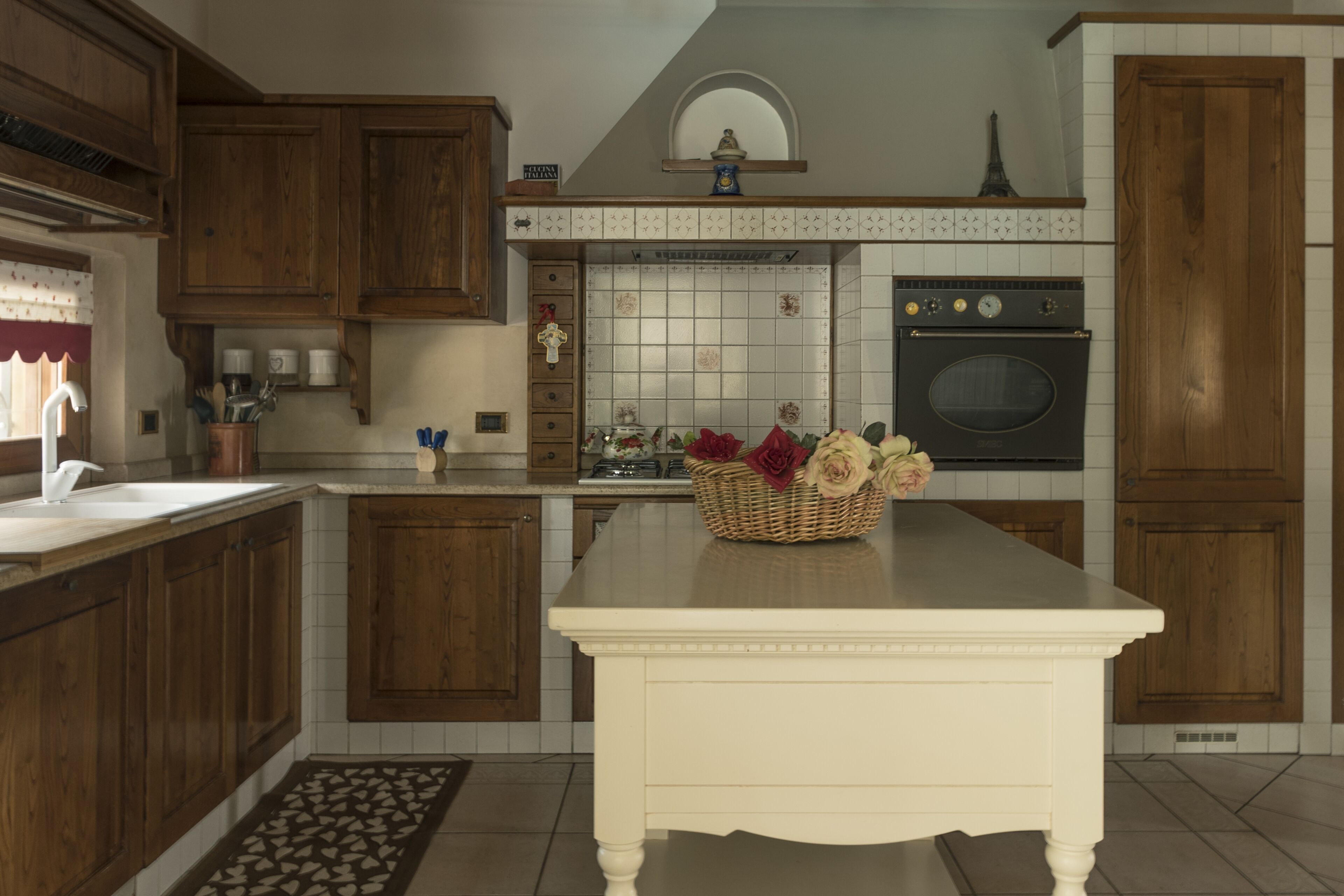 Una cocina con armarios de madera, encimera blanca y una isla central con un cesto de flores.