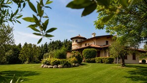 A large house with a stone tower, surrounded by a well-maintained lawn and various trees.