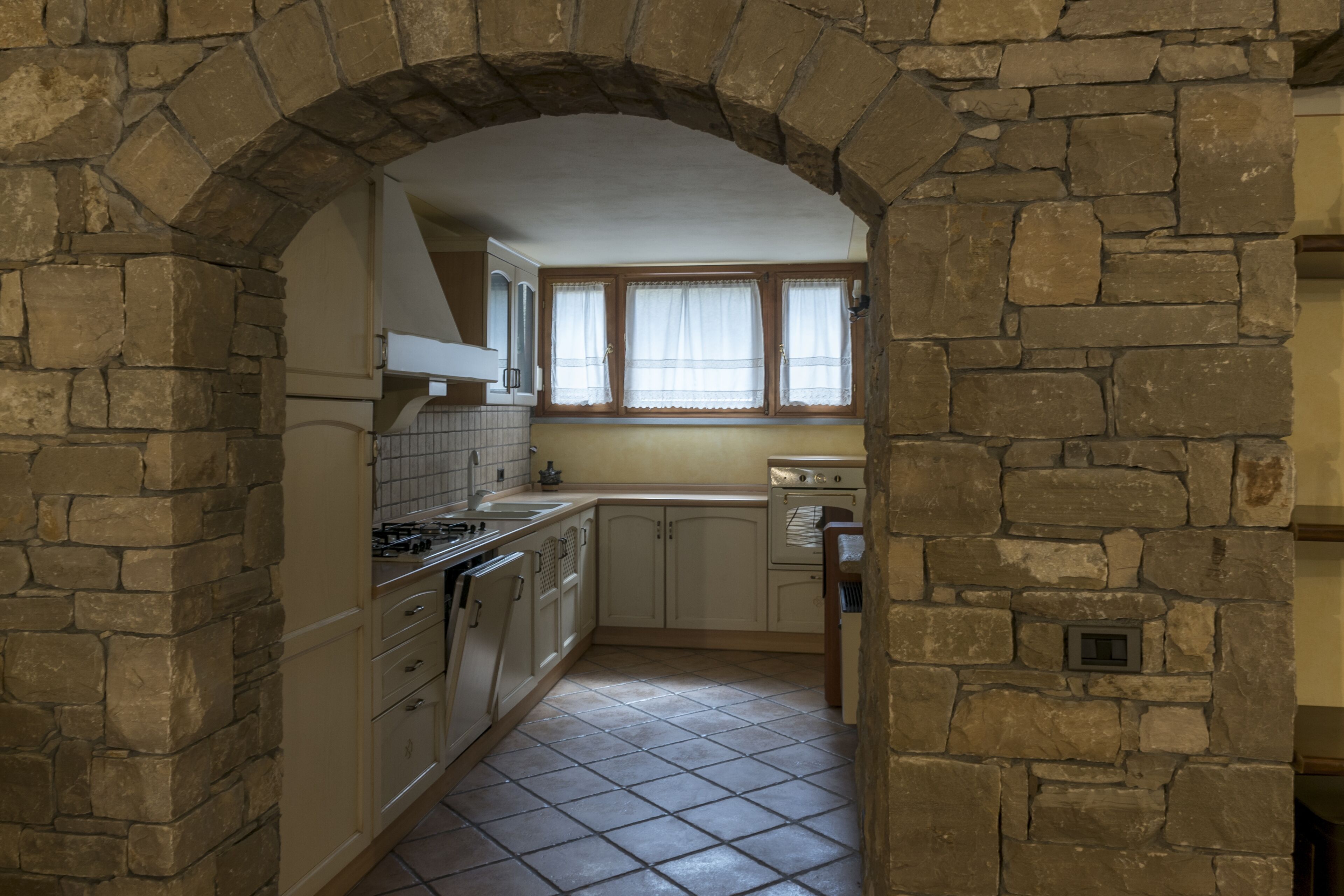A kitchen with stone walls, a tiled floor, and a window with curtains.