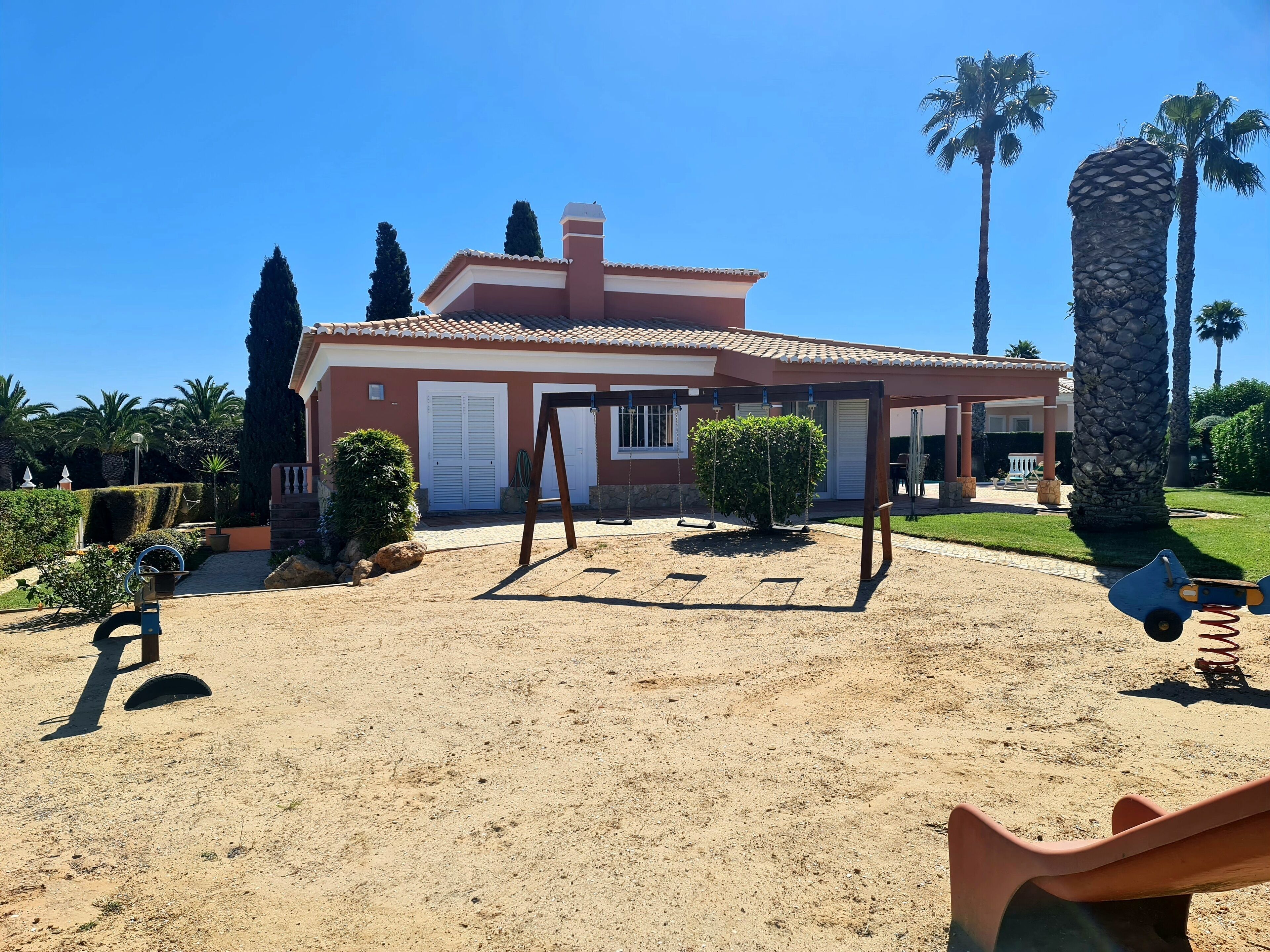A house with a patio, a swing set, and a palm tree.