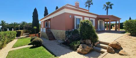 A house with a stone facade, a covered porch, and a well-maintained garden with grass and shrubs.