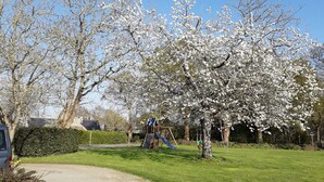 A park with a playground, including a slide and swings, surrounded by blooming trees. - LONGERE WITH COVERED AND HEATED SWIMMING POOL FOR 20 PEOPLE (EVELLYS)