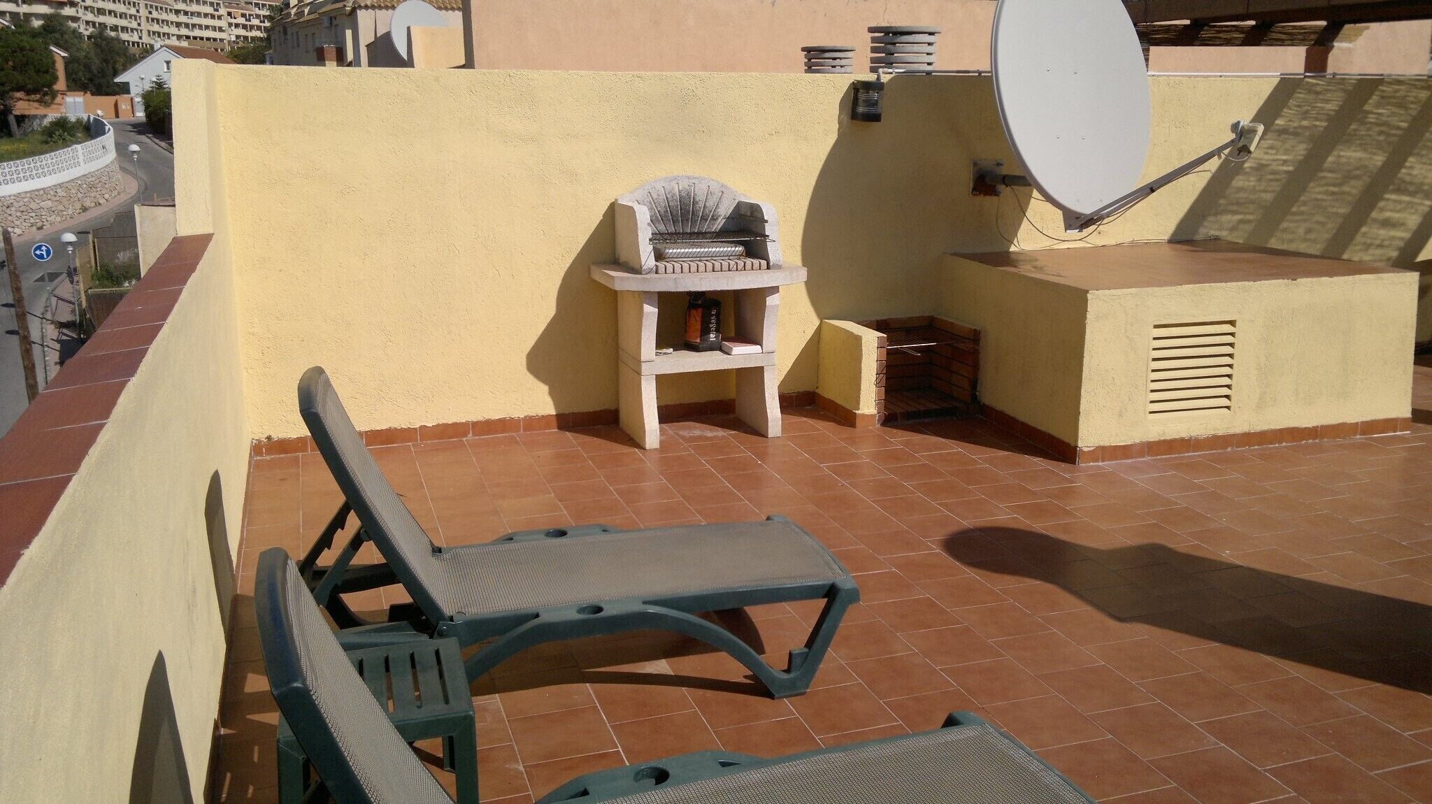 En takterrass med en grill, en satellitantenn och två solstolar.