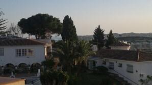 Zona residencial con una casa de techo a ladrillo, una torre de campanas y un árbol grande.