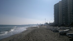 Una playa con una fila de tumbonas y un edificio alto al fondo.