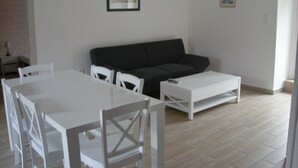 A living room with a white dining table, white chairs, a black sofa, and a white coffee table. -  Lodgings in Vannes (Plescop)