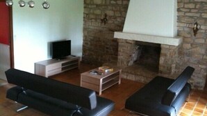 A living room with two black sofas, a coffee table, a TV, and a stone fireplace. -  Lodgings in Vannes (Plescop)