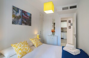 A hotel room with a bed, pillows, a bedside table with a lamp, a wardrobe, and a painting on the wall.