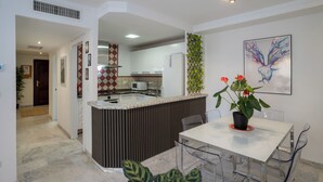 Una cocina moderna con armarios blancos, una isla central y un comedor con mesa y sillas blancas.