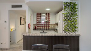 Cocina compacta con una isla central, microondas y pileta. Posee un salpicadero con diseño y una pared decorativa con plantas verdes.