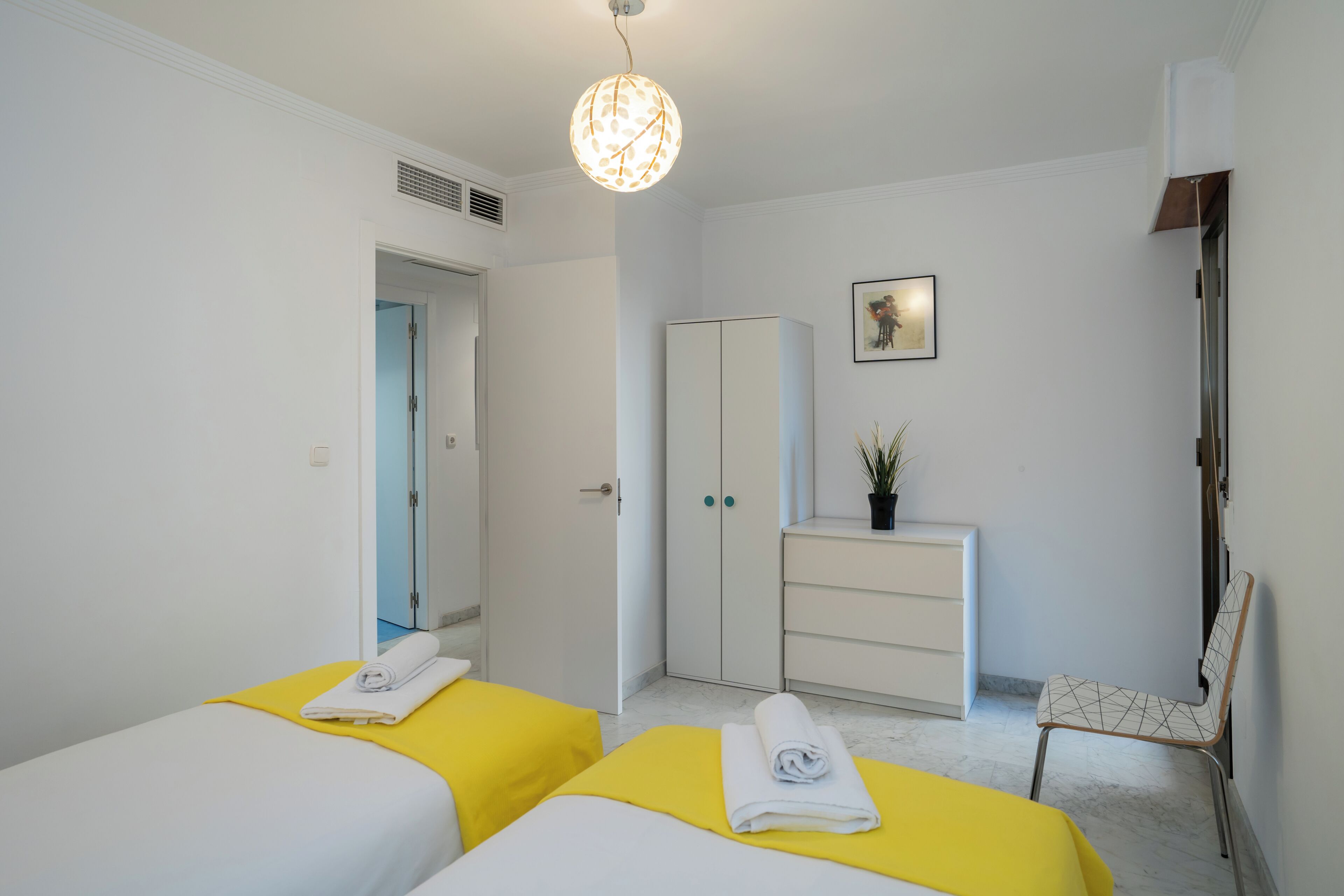 Une chambre d’hôtel avec deux lits, une armoire, une chaise et un luminaire au plafond.