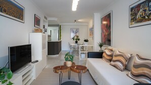 Una sala moderna con un televisor de pantalla plana, un sofá, una mesa de centro y un comedor al fondo.