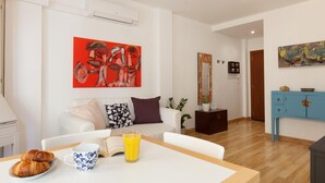 A modern living room with a white sofa, a coffee table with croissants and a coffee cup, and a painting on the wall. - ATTRACTIVE APARTMENT IN COSTA BRAVA (Tossa de Mar)