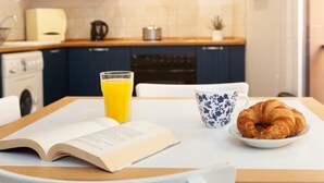 A breakfast setting with a book, a glass of orange juice, a blue floral cup, and a croissant on a white plate. - ATTRACTIVE APARTMENT IN COSTA BRAVA (Tossa de Mar)