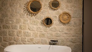 Een badkamer met een vrijstaand bad, een stenen muur en decoratieve spiegels.