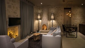 Een moderne woonkamer met een stenen muur, een open haard, een flatscreen televisie en een eethoek met een tafel en stoelen.
