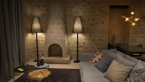 Een gezellige woonkamer met een stenen muur, een open haard, een bank met decoratieve kussens en twee vloerlampen.