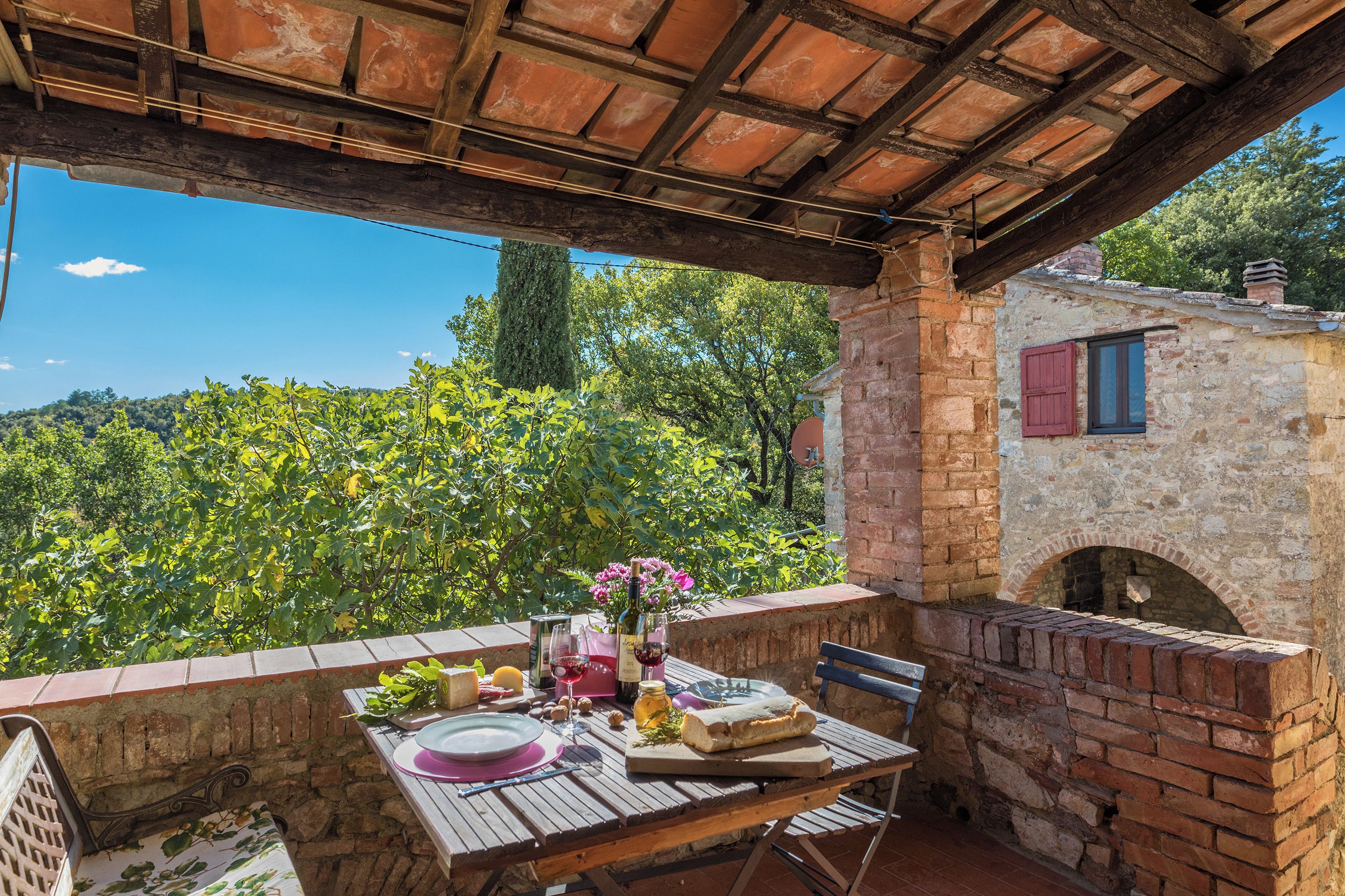 A rustic outdoor dining area with a brick table, a wine bottle, and a view of a vineyard.