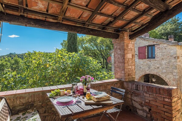 A rustic outdoor dining area with a brick table, a wine bottle, and a view of a vineyard.