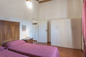 Une chambre à coucher avec une tête de lit en bois, un lit recouvert d’une couvre-lit à motifs floraux, une table de chevet avec une lampe et une armoire.