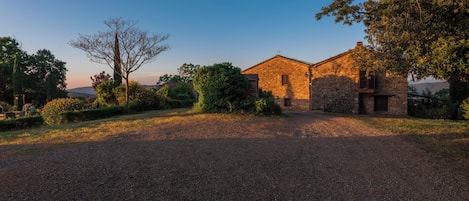 Un edificio de piedra con camino de grava, rodeado de árboles y arbustos.