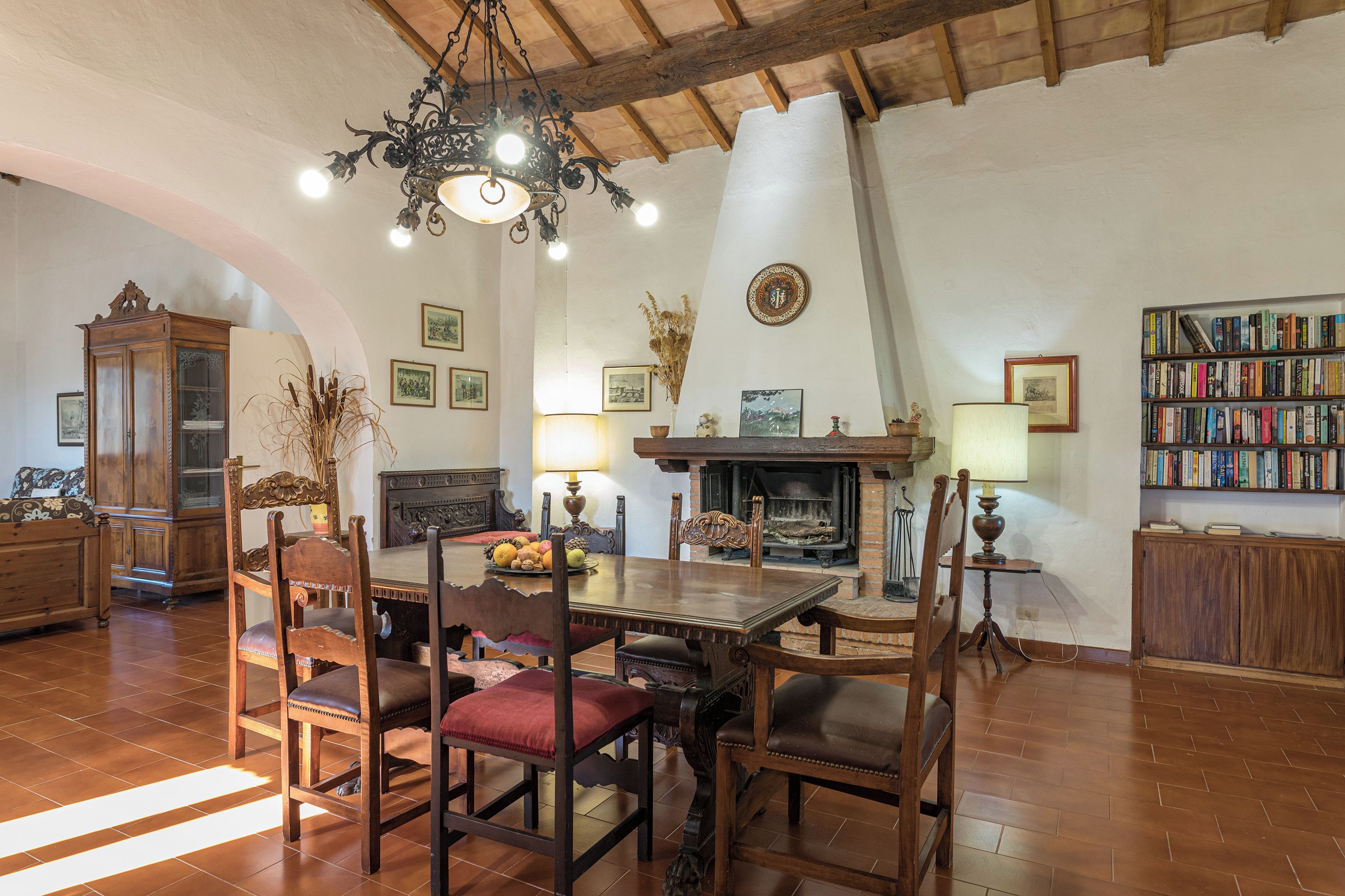 Un salon chaleureux avec une table à manger en bois, des chaises, une cheminée, des étagères et un lustre.