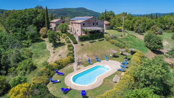 Une propriété dotée d’une piscine, de plusieurs chaises longues et d’un bâtiment en pierre avec un jardin.