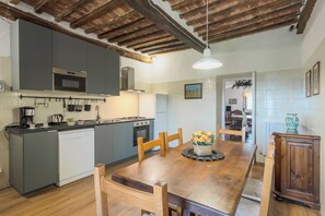 Une cuisine compacte dotée d’appareils électroménagers modernes, un coin repas avec une table en bois et une vue sur le salon.