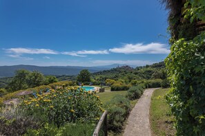 A pool area with lounge chairs, surrounded by greenery and a clear view of distant hills.