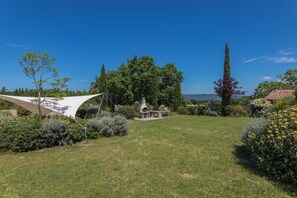 Un jardin agrémenté d’un banc en pierre, d’une pergola et de diverses plantes.