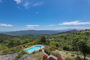 Une piscine entourée de verdure et, au loin, un bâtiment perché sur une colline.
