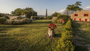 A rural landscape with a stone building, a white tent-like structure, and a tree stump with red flowers.