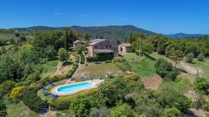 A large house with a swimming pool surrounded by greenery and hills in the background.