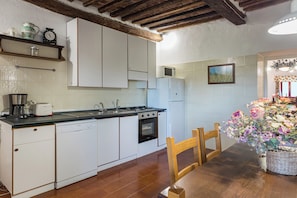 A compact kitchen with white cabinets, a stove, and a sink. There is a dining table with chairs and a vase of flowers. - Woodland Cottage (A3) with pool - Le Caldanelle (Civitello Paganico, Grosseto)