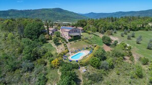 Une villa avec piscine, entourée d’une végétation luxuriante et avec des collines en arrière-plan.