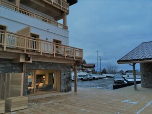 Un edificio de varios pisos con fachada de piedra, balcones de madera y un área exterior cubierta con nieve en el suelo.