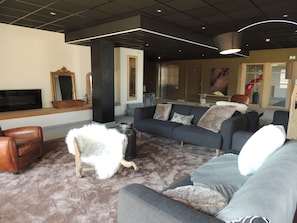 Ein modernes Wohnzimmer mit einem grauen Sofa, einem braunen Ledersessel, einem weißen, flauschigen Ottomanen und einem flachbildfernseher an der Wand.