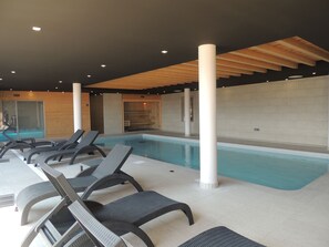 Ein Hallenbad mit Liegestühlen und einer Sauna-Bereich.